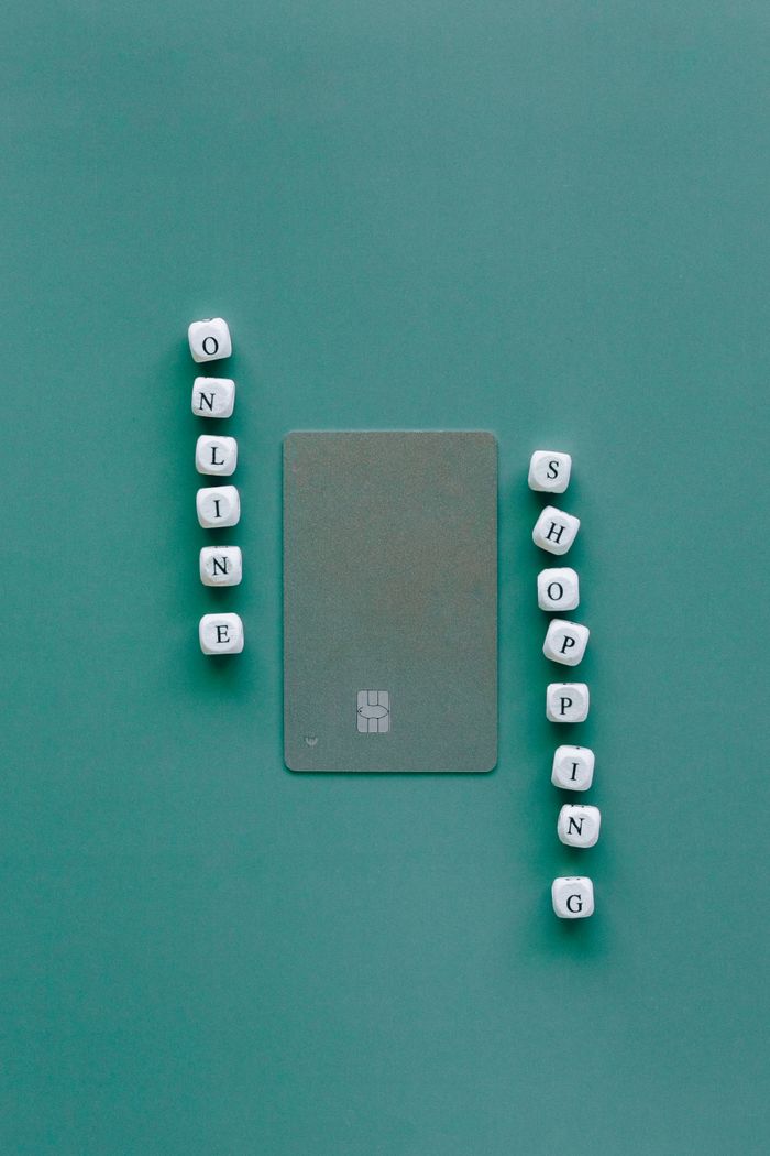 Flat lay with credit card surrounded by word Online Shopping on green backdrop.
